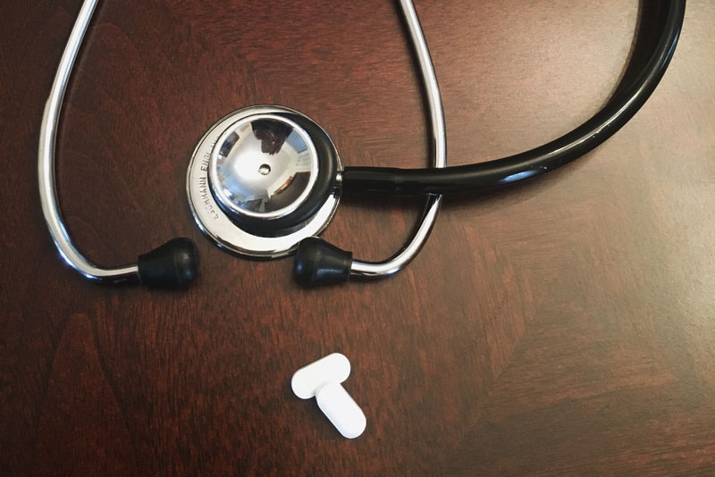 A stethoscope and pills on a wooden desk